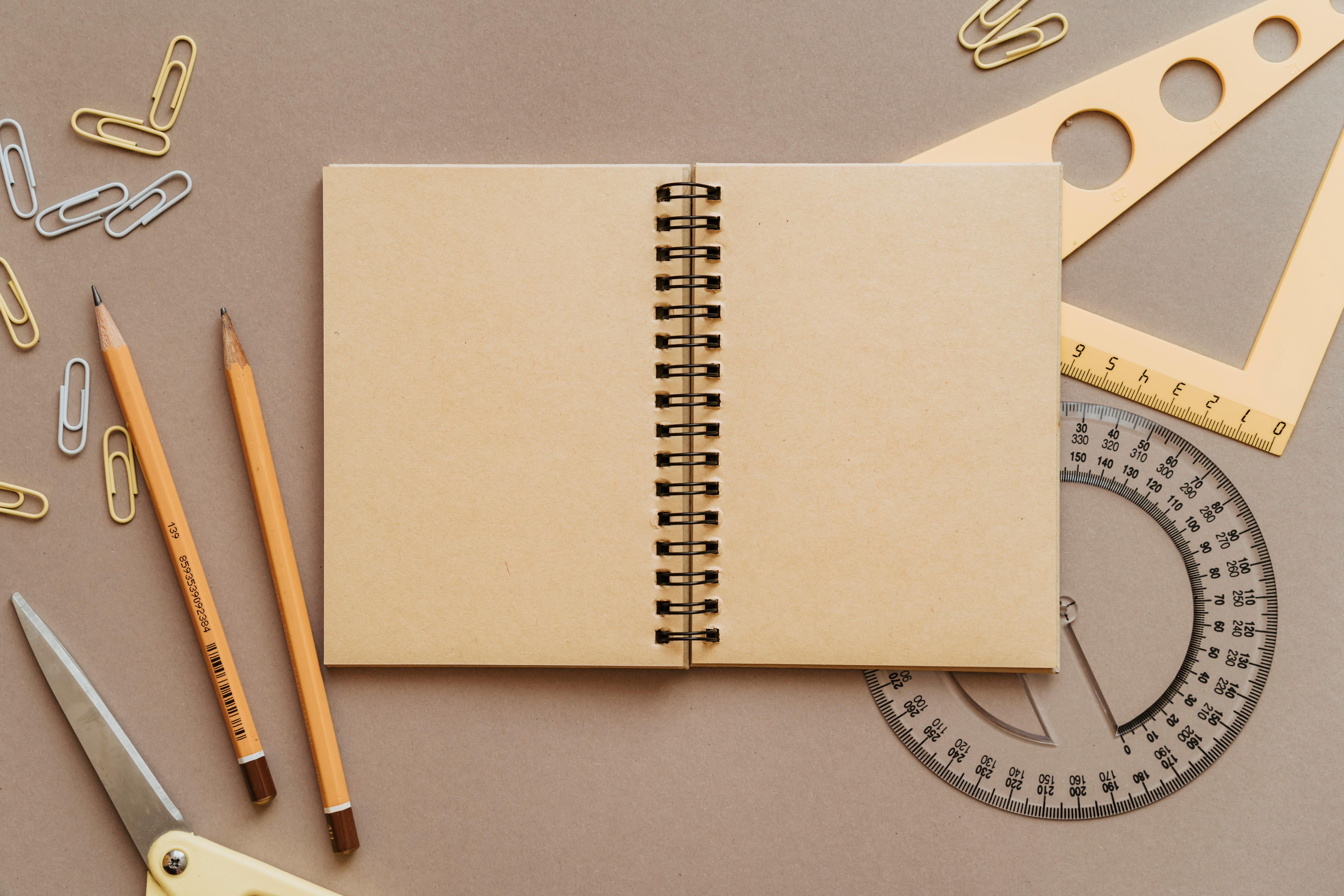 Open spiral-bound notebook with scissors, pencils, and measuring tools on a craft surface