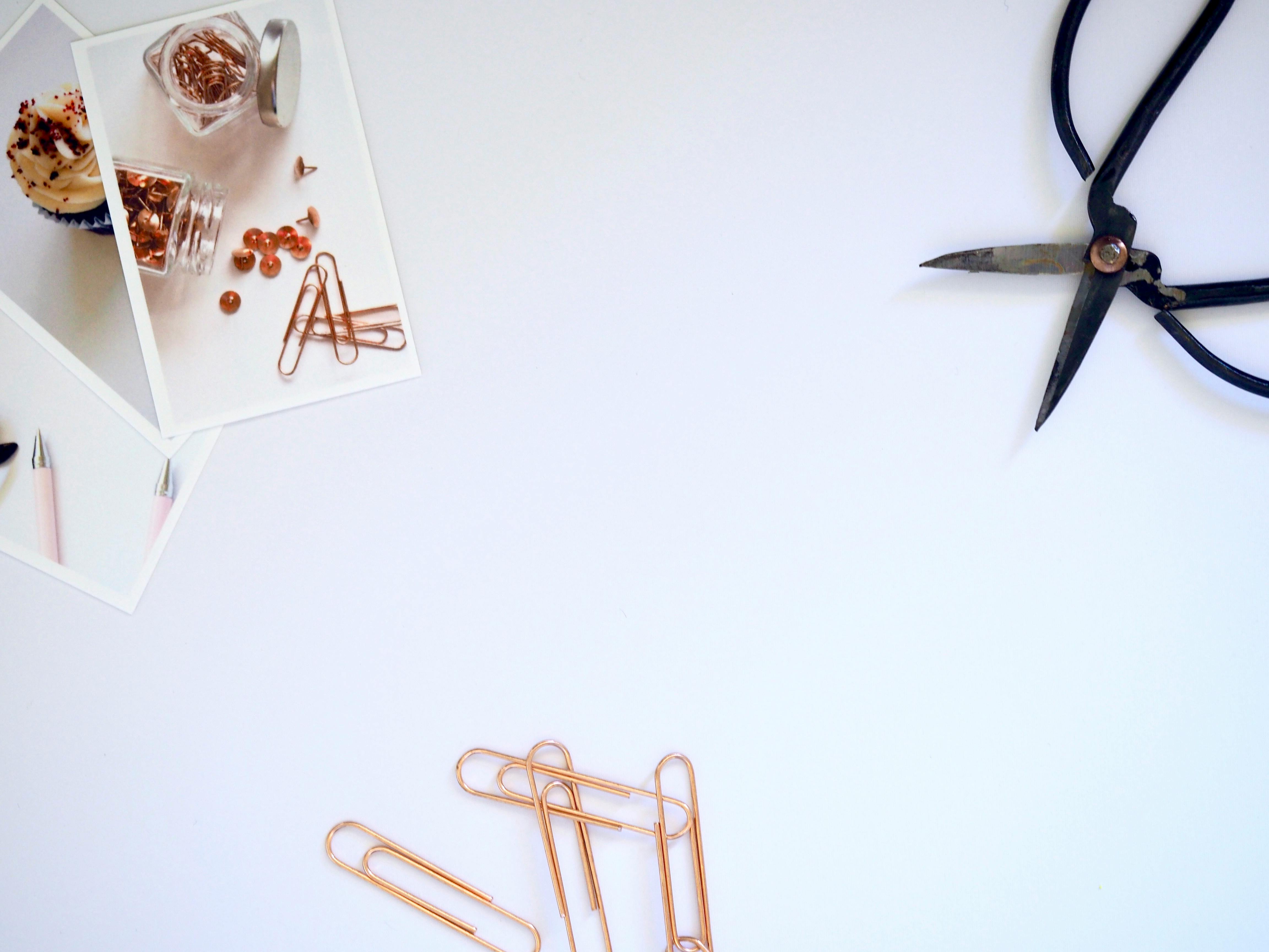 Flat lay of photo prints, paper clips, and scissors on a white desk